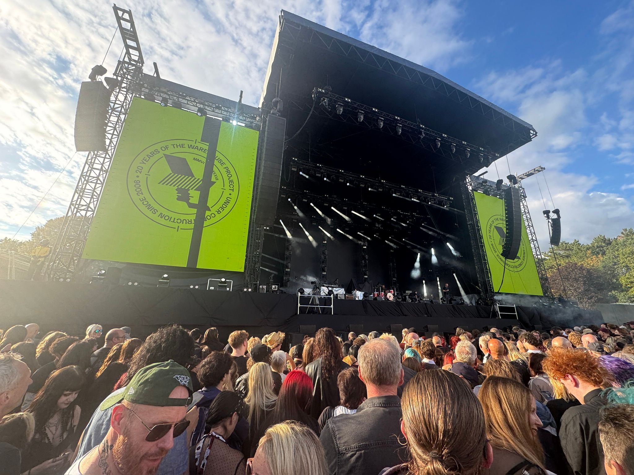 A large stage with two screens on either side, and a throng of people gathered at the foot of it, extending along the bottom of the photo