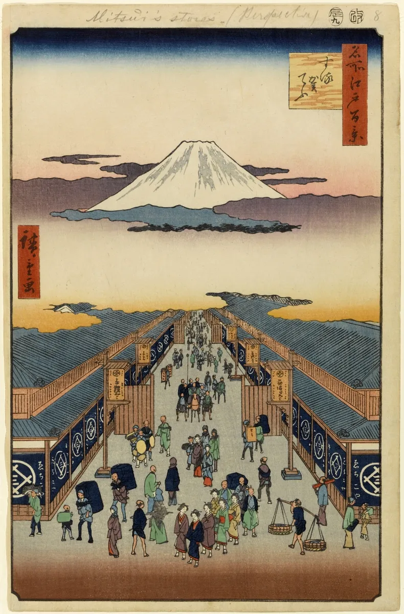 A bustling town street full of people, with the snow-covered peak of Mount Fuji looming large in the distance.