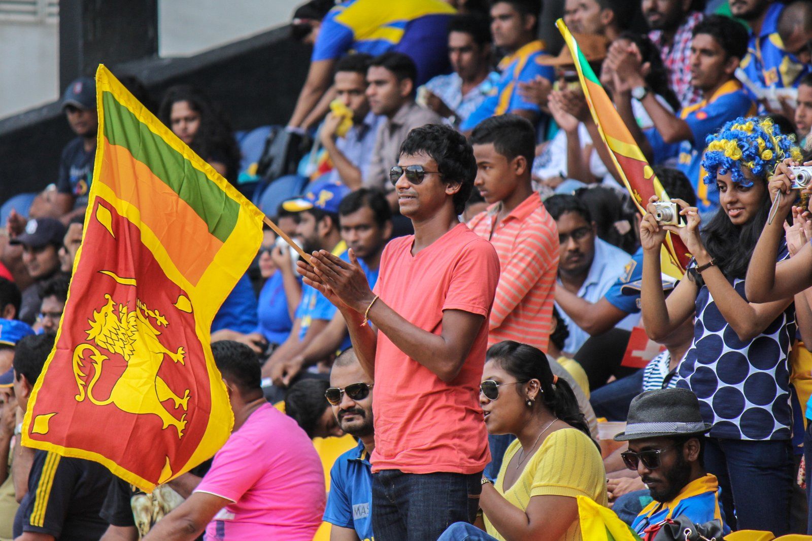 A crowd consisting of Sri Lankan fans at a cricket match, holding Sri Lankan flags and pointing cameras