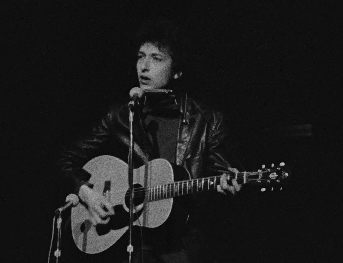 A black and white photo of a young Bob Dylan performing with his guitar
