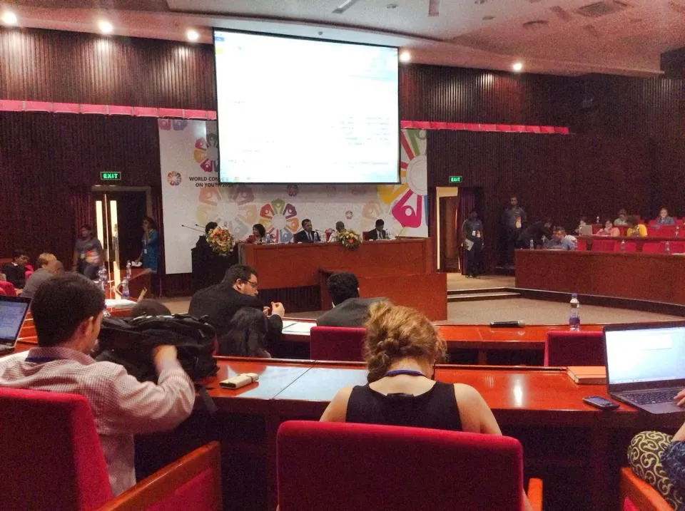 A head table at a large conference room with delegates gathered around it, seated in a circular conference arrangement