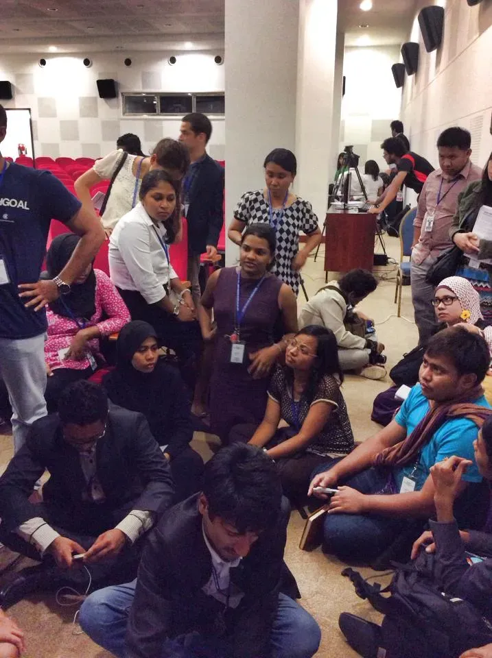 Delegates sitting on the ground and listening to a presenter