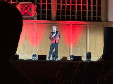 James Acaster on stage, wearing a red jacket