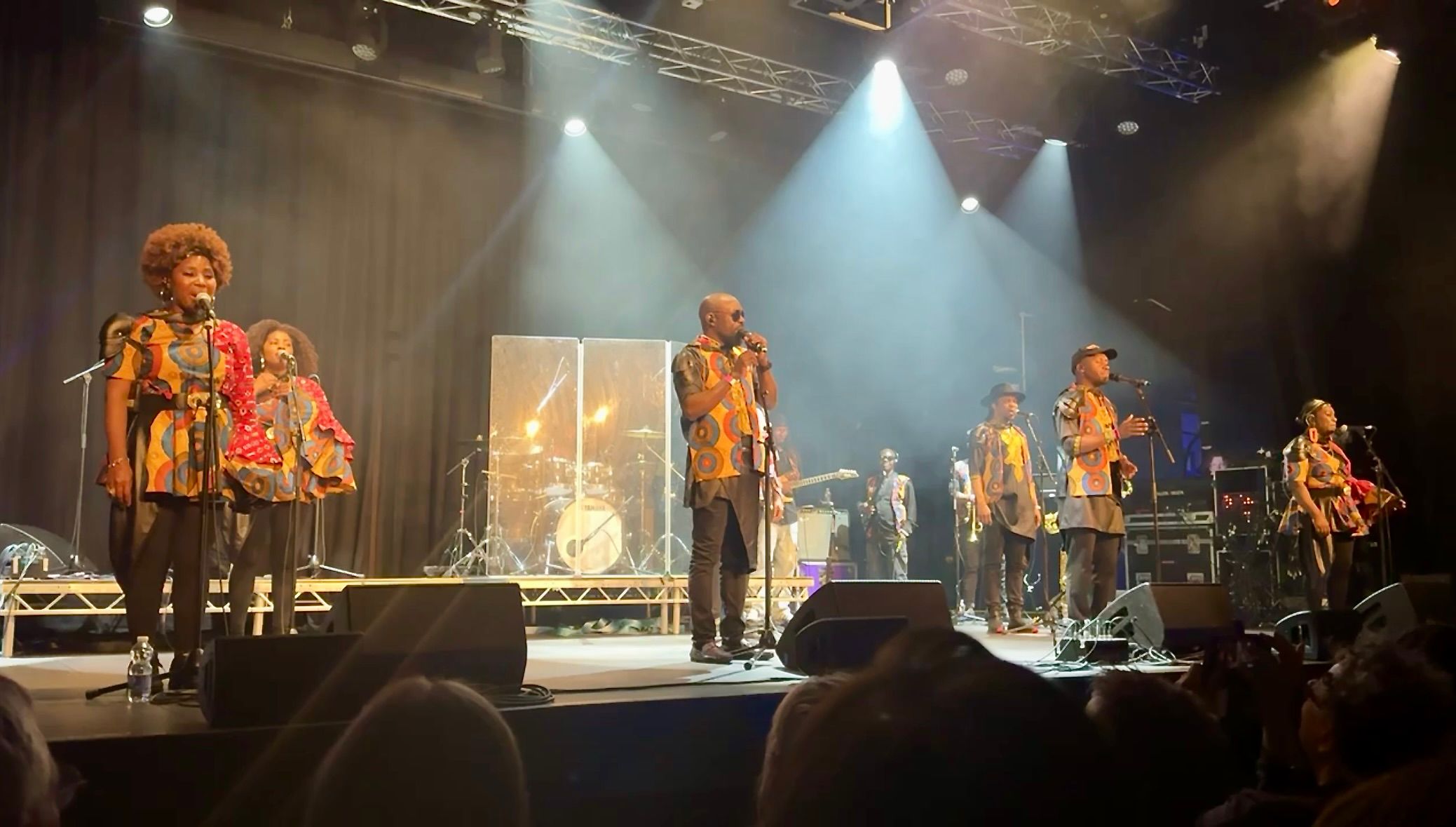 The many memebers of the London African Gospel Choir performing on a stage illuminated by bright lists