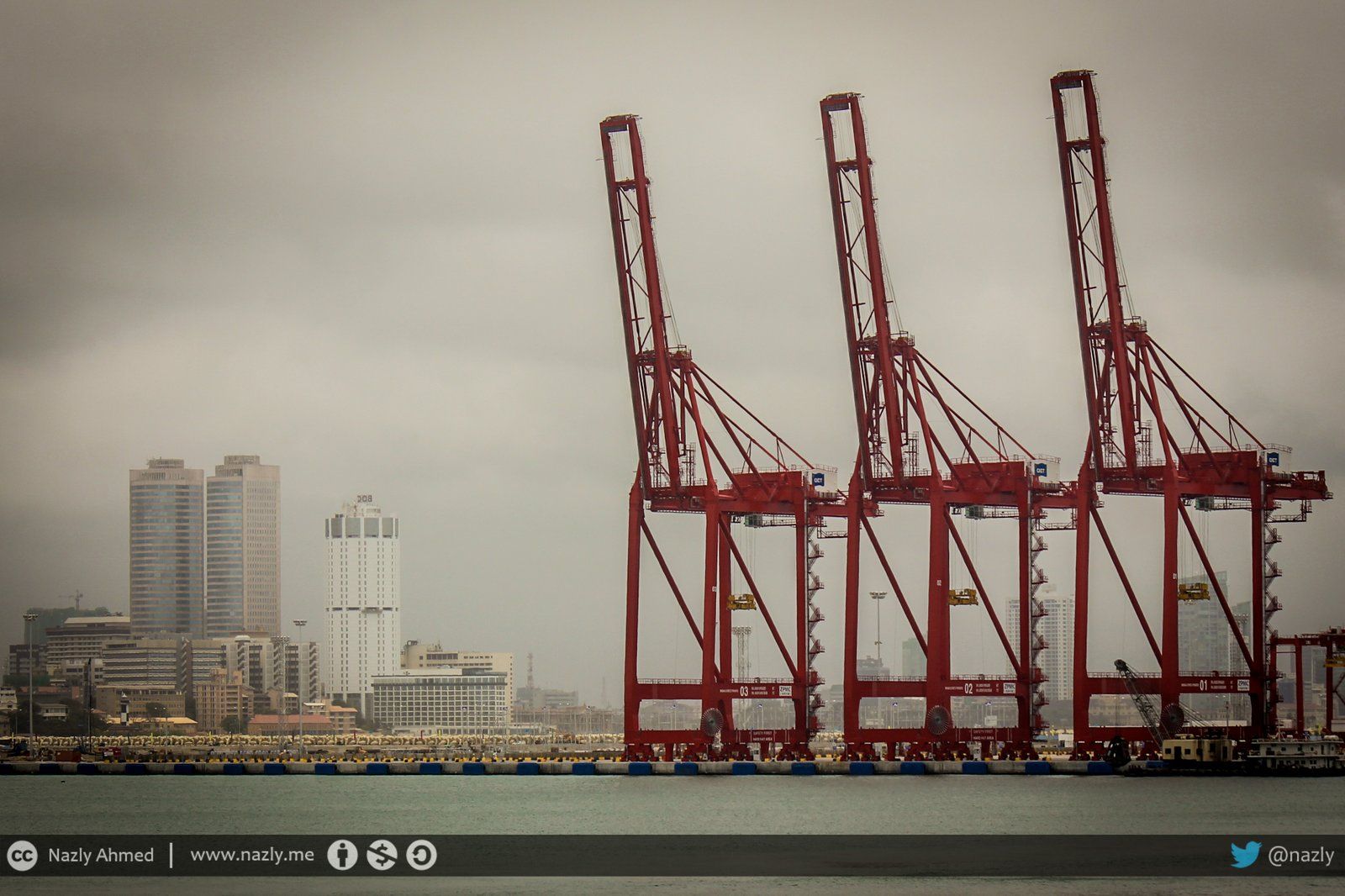 3 large red cranes of the Colombo port in the foreground with the city skyline in the background