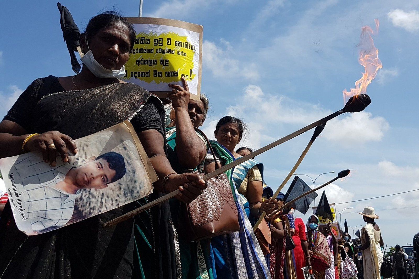 A group of women protesting the enforced disappearances of their loved ones; they are holding lit torches, placards and photos of the victims
