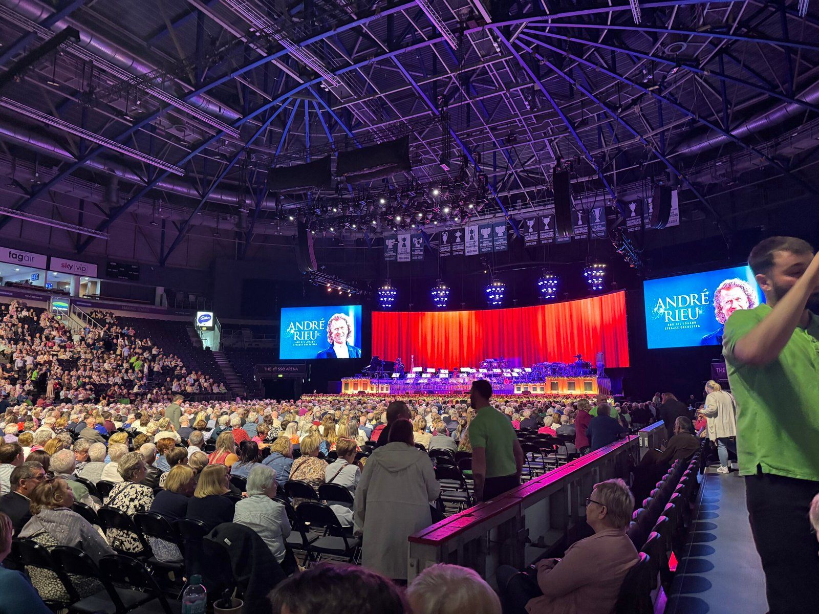 A photo of the SSE Arena stage, just before the orchestra went on. There are two large screens on either side of the stage, and the audience looks on in anticipation.