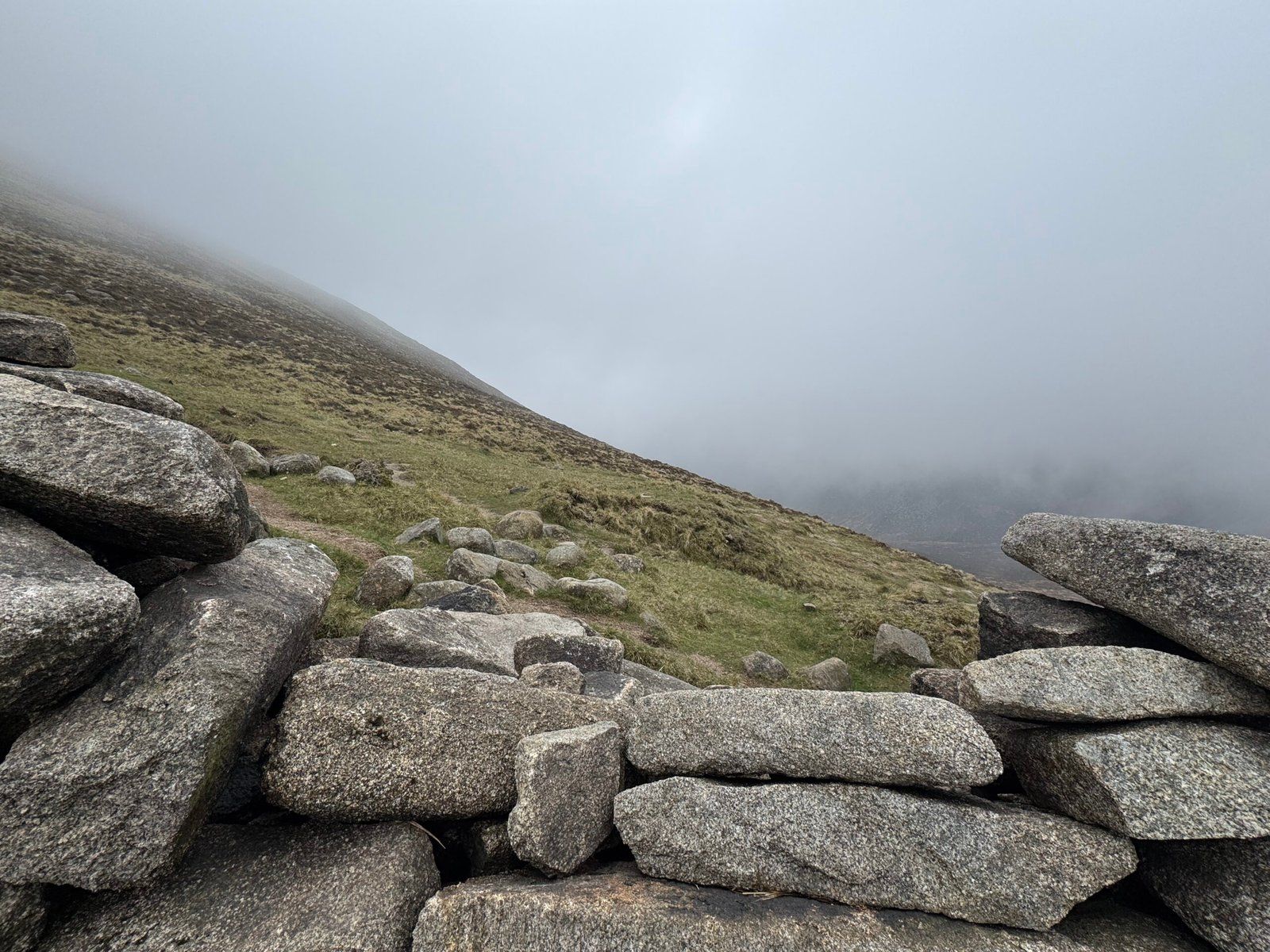 The mountainside covered in mist, as seen through the opening in a rock wall
