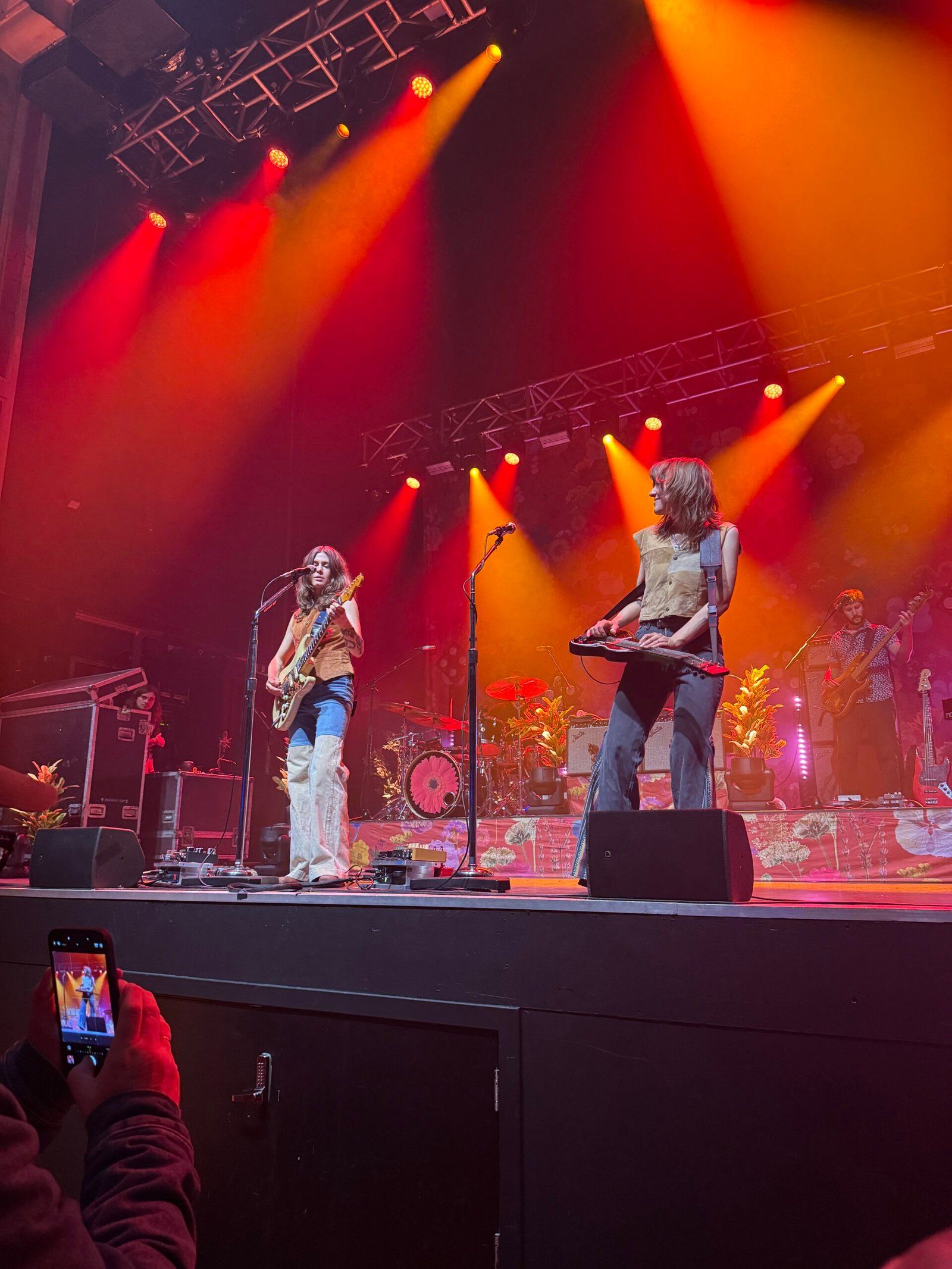 Rebecca (left) and Megan Lovell (right) on stage peforming. Rebecca is playing an electric guitar and Megan is playing a lap steel. The rest of the band can be seen in the background.