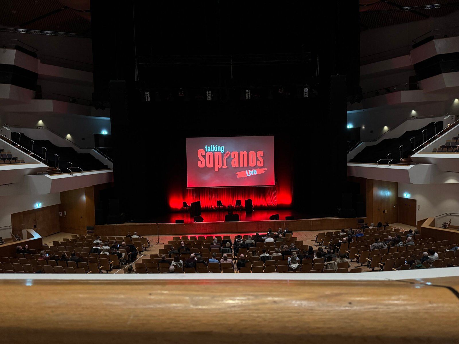A photo of the Talking Sopranos stage, a few minutes before the event began. The logo of the podcast is projected on to a screen on the stage, which is backlit in red.