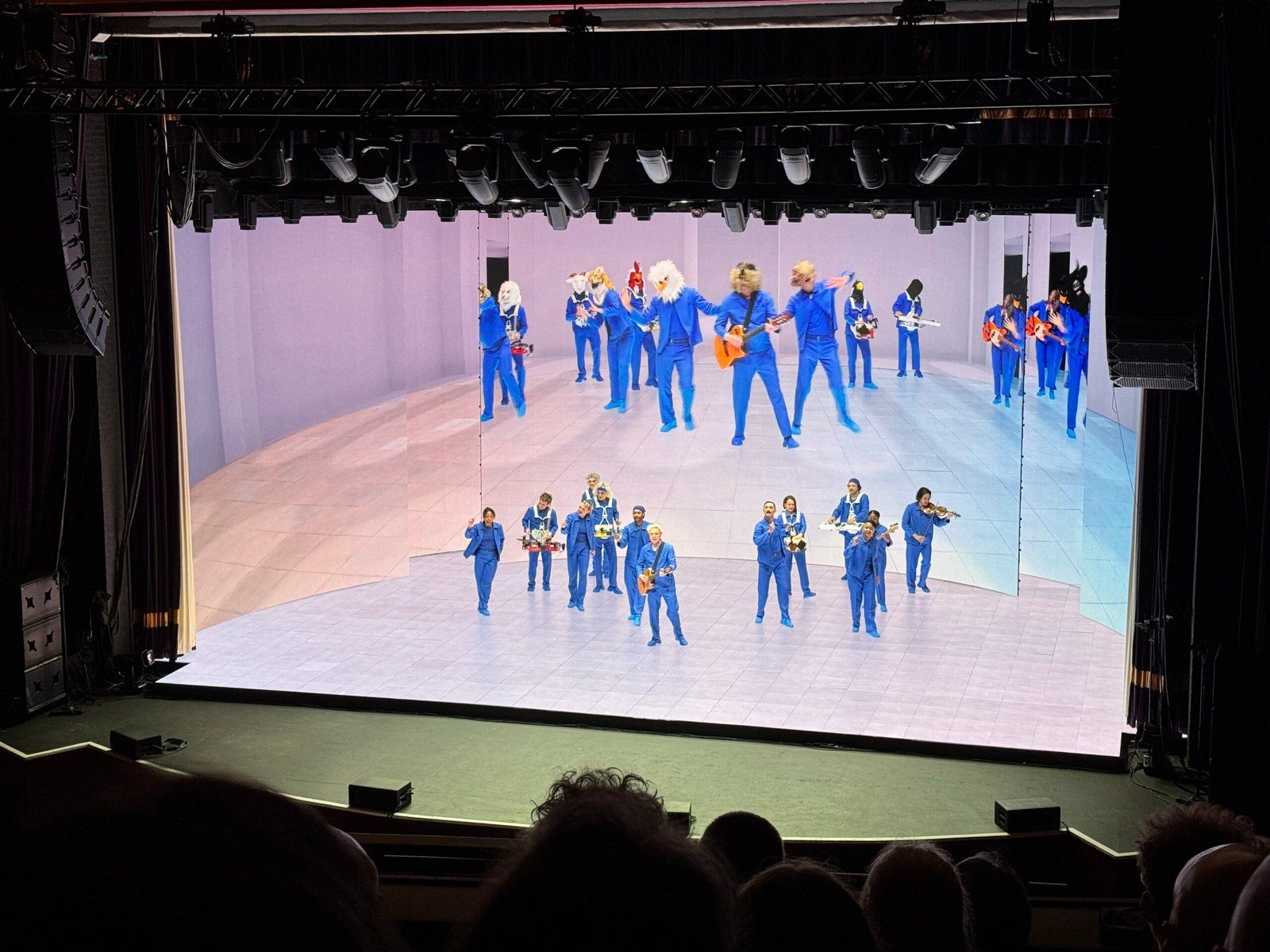David Byrne and the crew performing on stage. They're all wearing blue; some are playing musical instruments and some are dancing.
