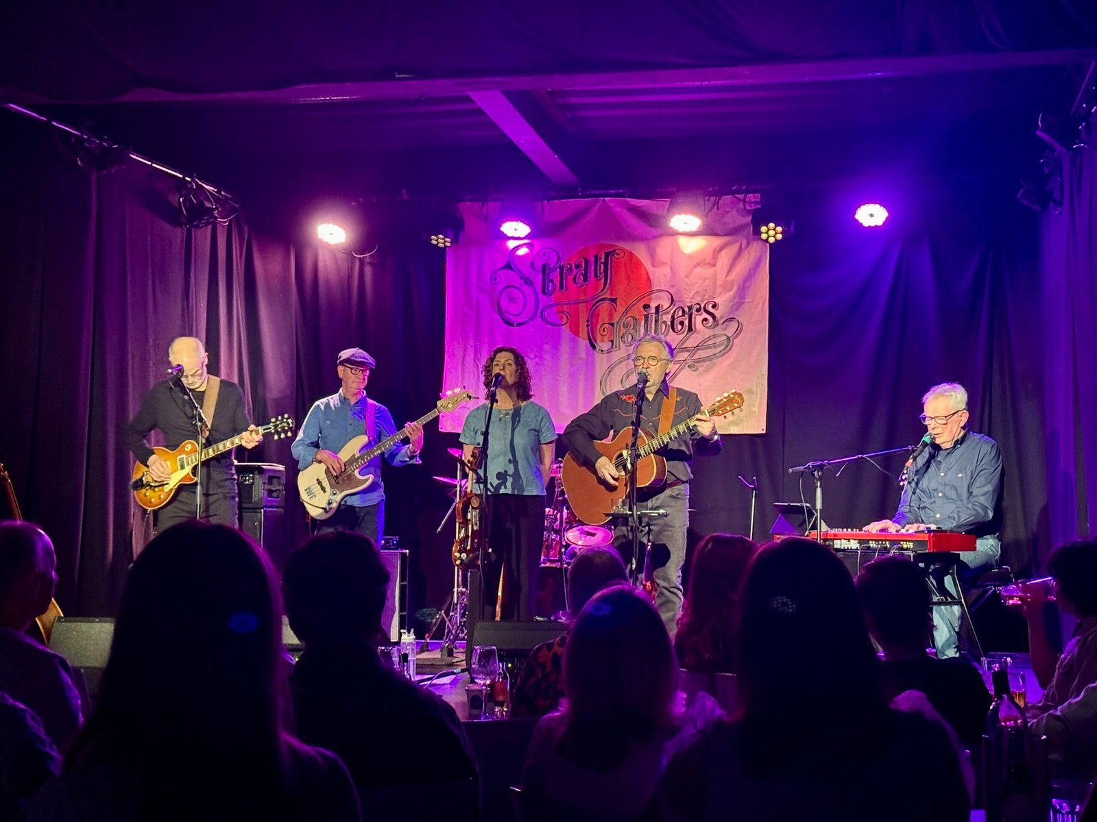 The Stray Gaiters on stage, from left to right: lead guitar, bass guitar, vocals, vocals and guitar, and keyboards.