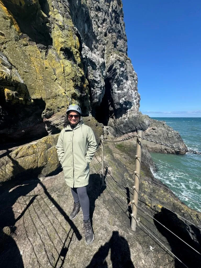 A photo of Nuwani standing next to the protective fence at the end of the path. She is wearing a green coat, a hard hat and sunglasses.
