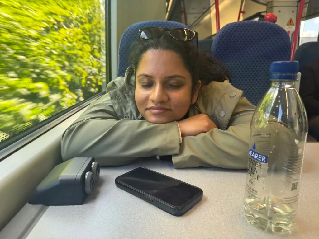 Nuwani sleeping on the train. She is resting her face against her forearms on top of a table.