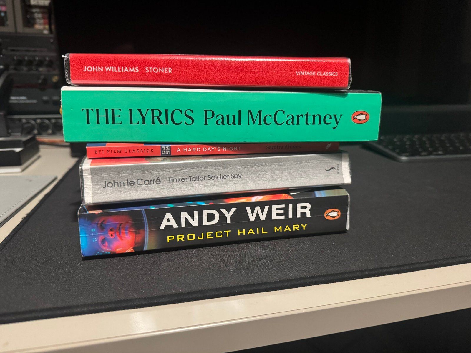 Some books from my reading list, stacked on top of each other. From top to bottom: Stoner, The Lyrics, A Hard Day's Night, Tinker Tailor Soldier Spy, and Project Hail Mary.