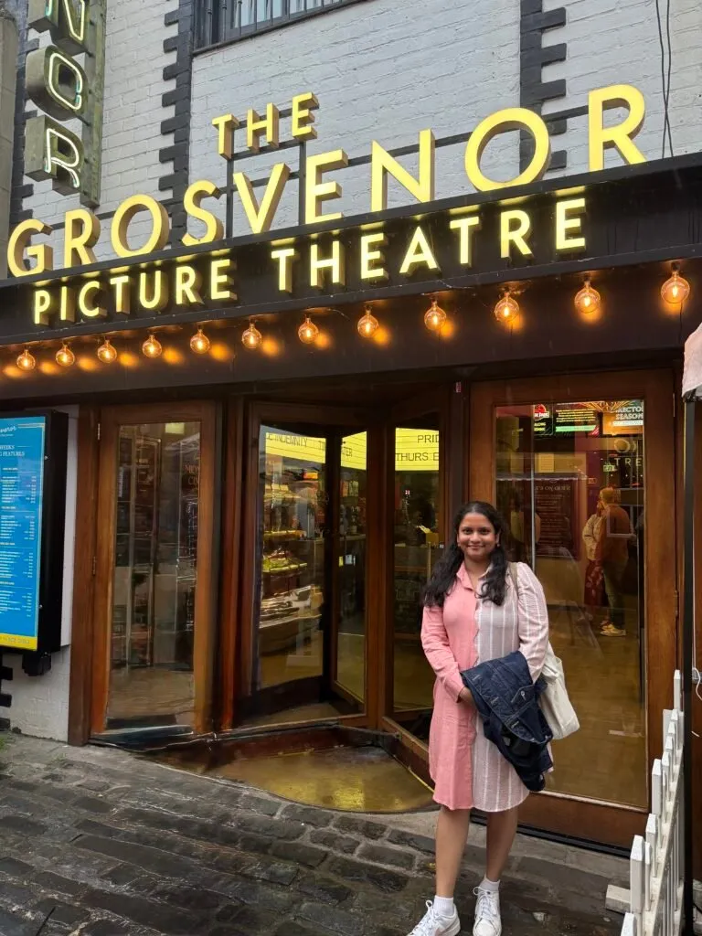 Nuwani posing outside the cinema, under the large illuminated sign that reads The Grosvenor Picture Theatre.
