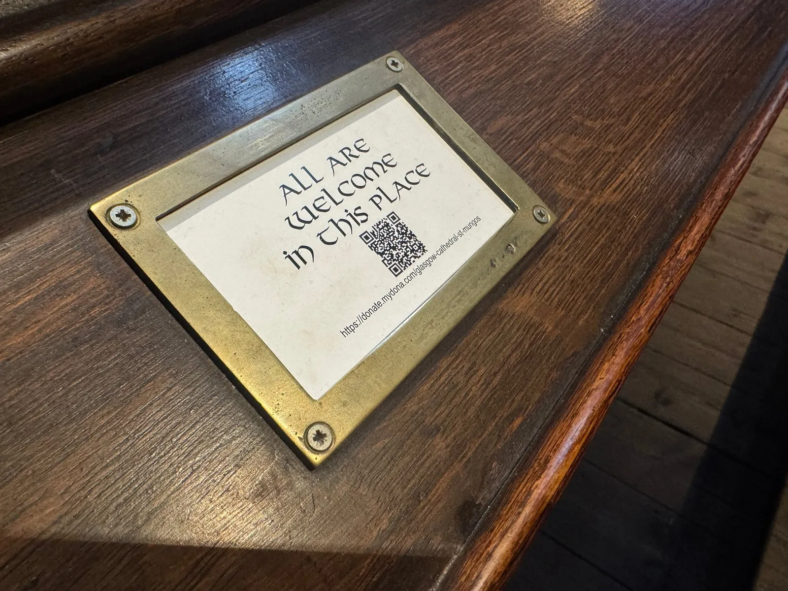 A sign that reads “all are welcome in this place” which is displayed on the pews.