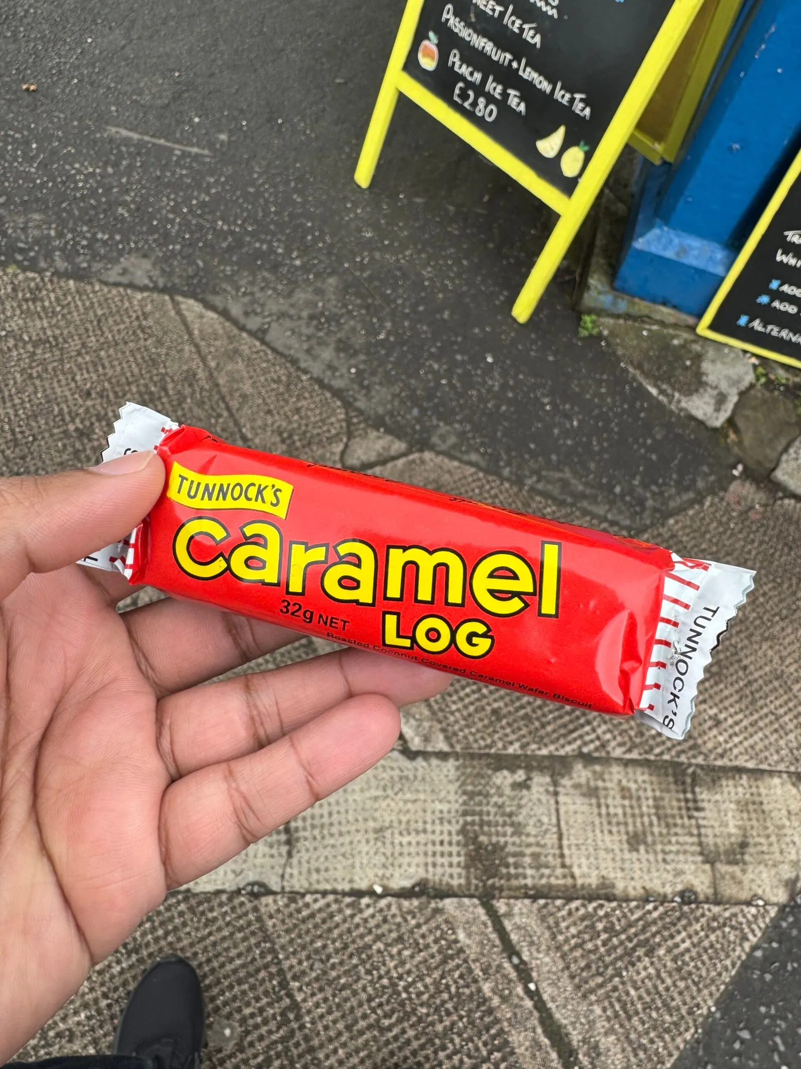 Me holding a Tunnock’s Caramel Log, a chocolate and caramel covered wafer treat, in a red and white wrapper.