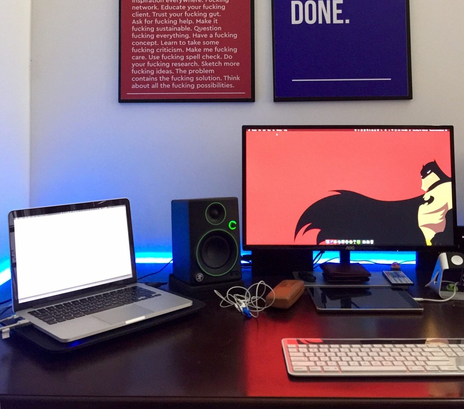Desk setup featuring a latop on the left and a monitor on the right. There is a speaker between them, and two posters hanging on the wall behind them.