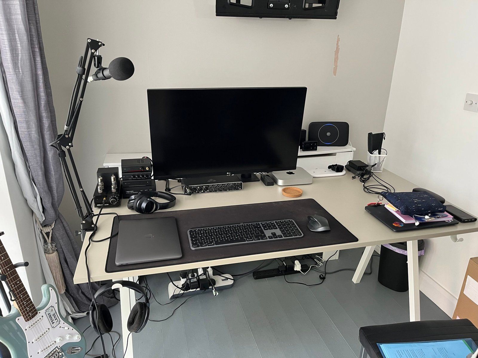 Desk setup featuring a monitor, laptop, wireless keyboard and mouse, mic, headphone setup, and other peripherals