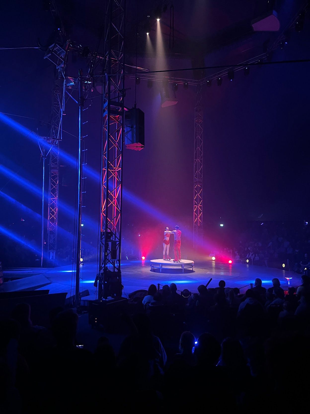 Two performers, wearing red, about to start their peformance on a stage lit in pruple and blue light