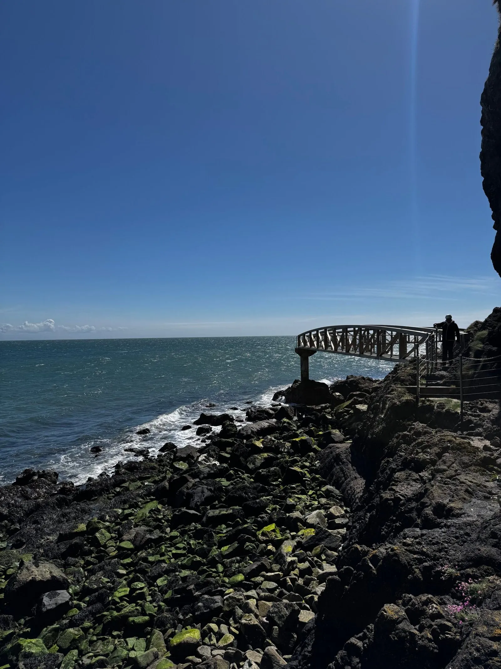 Two bridges intersecting at a concrete column built into the rocky shore, with the horizon in the background.