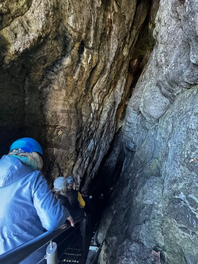 A group of people, all wearing hard hats, descending a staircase leading into a cave