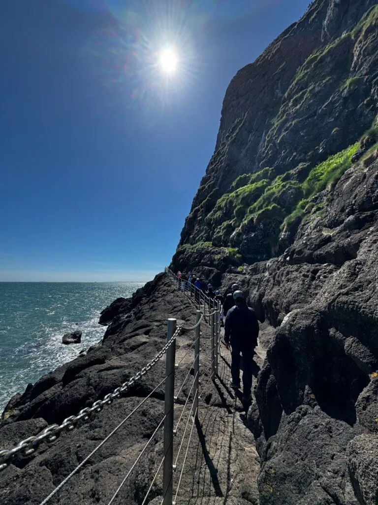 People walking along the path, with the sea on the left and a sheer cliff face on the right.