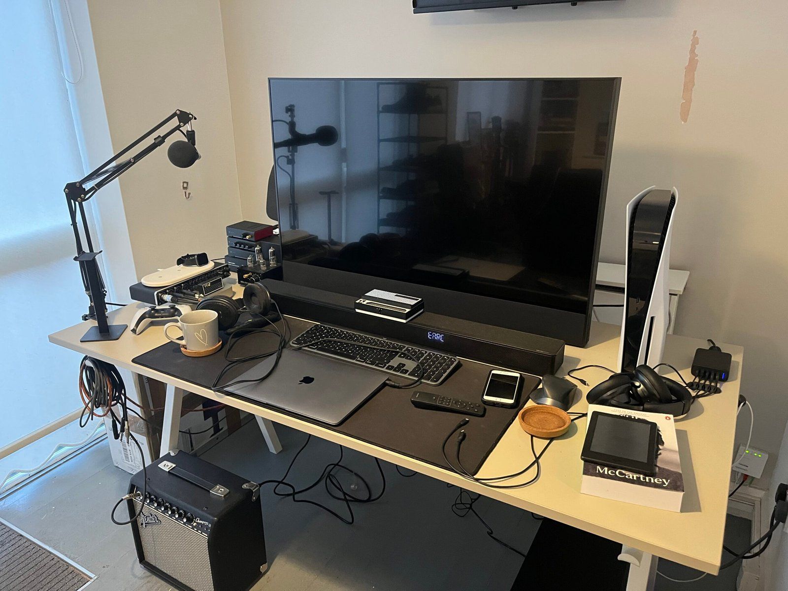 Desk setup featuring a medium TV, soundbar, PS5, mic, laptop, headphone setup and other peripherals