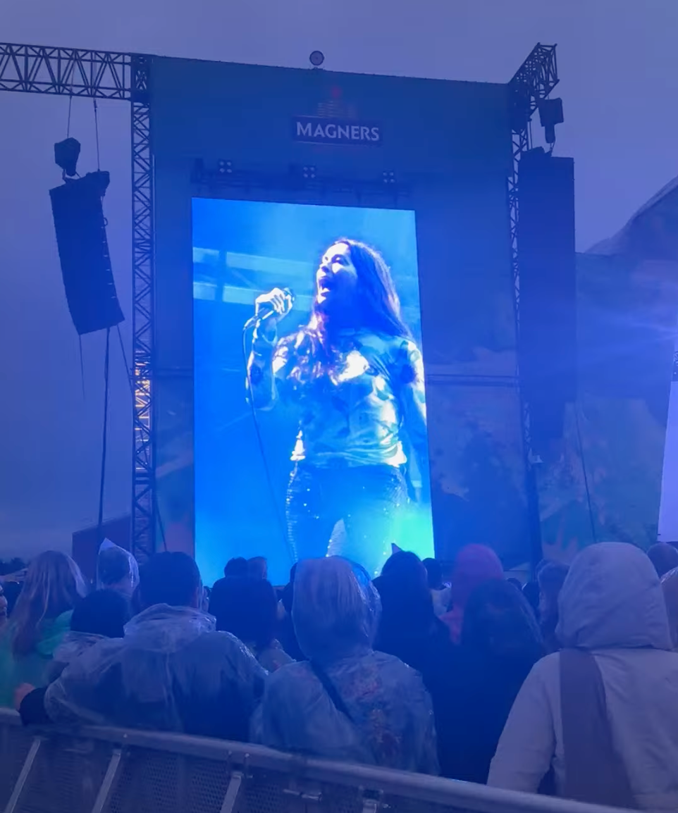 Alanis singing into a mic, as seen through a large screen on the side of the stage