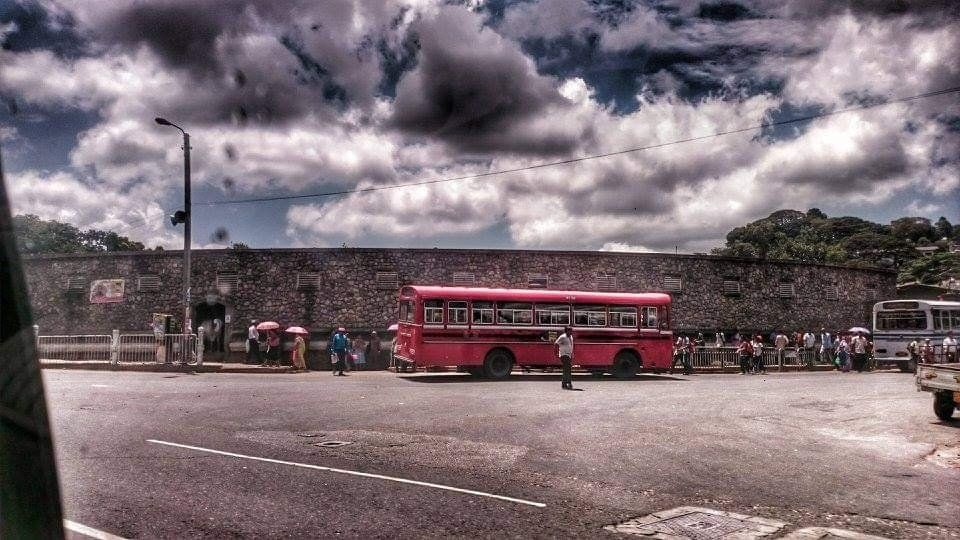 A red CTB bus parked against a wall, with people milling about, in Colombo, Sri Lanka.