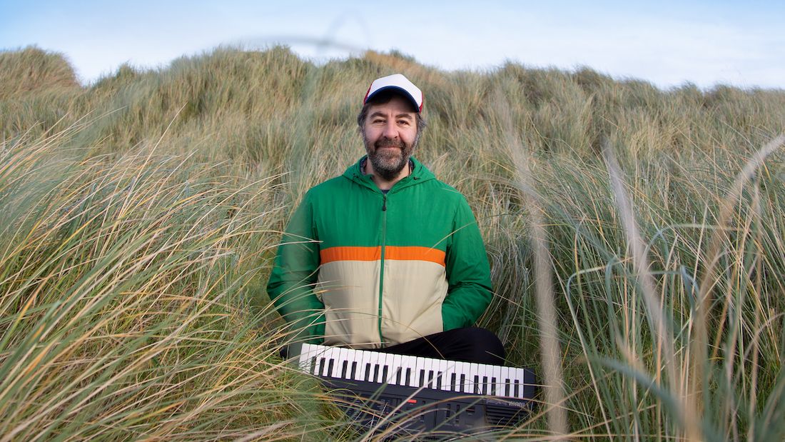 A promotional photo of David with his keyboard standing in a field of tall grass