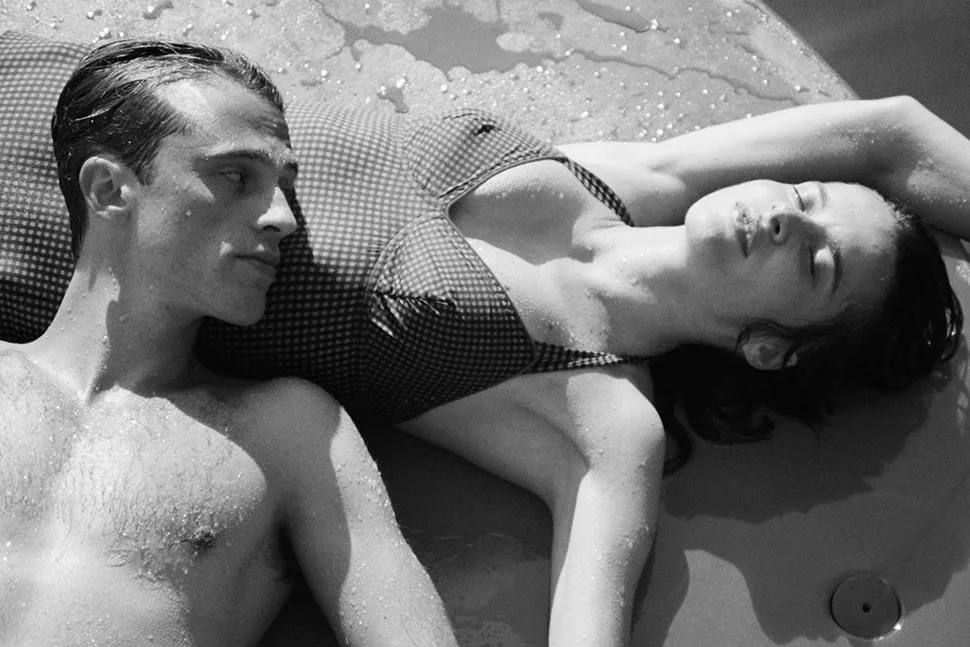 Benjamin Voisin and Rebecca Marder in a still from the The Stranger, the former laying his head on the latter’s torso, looking at her as she sunbathes with her eyes closed.