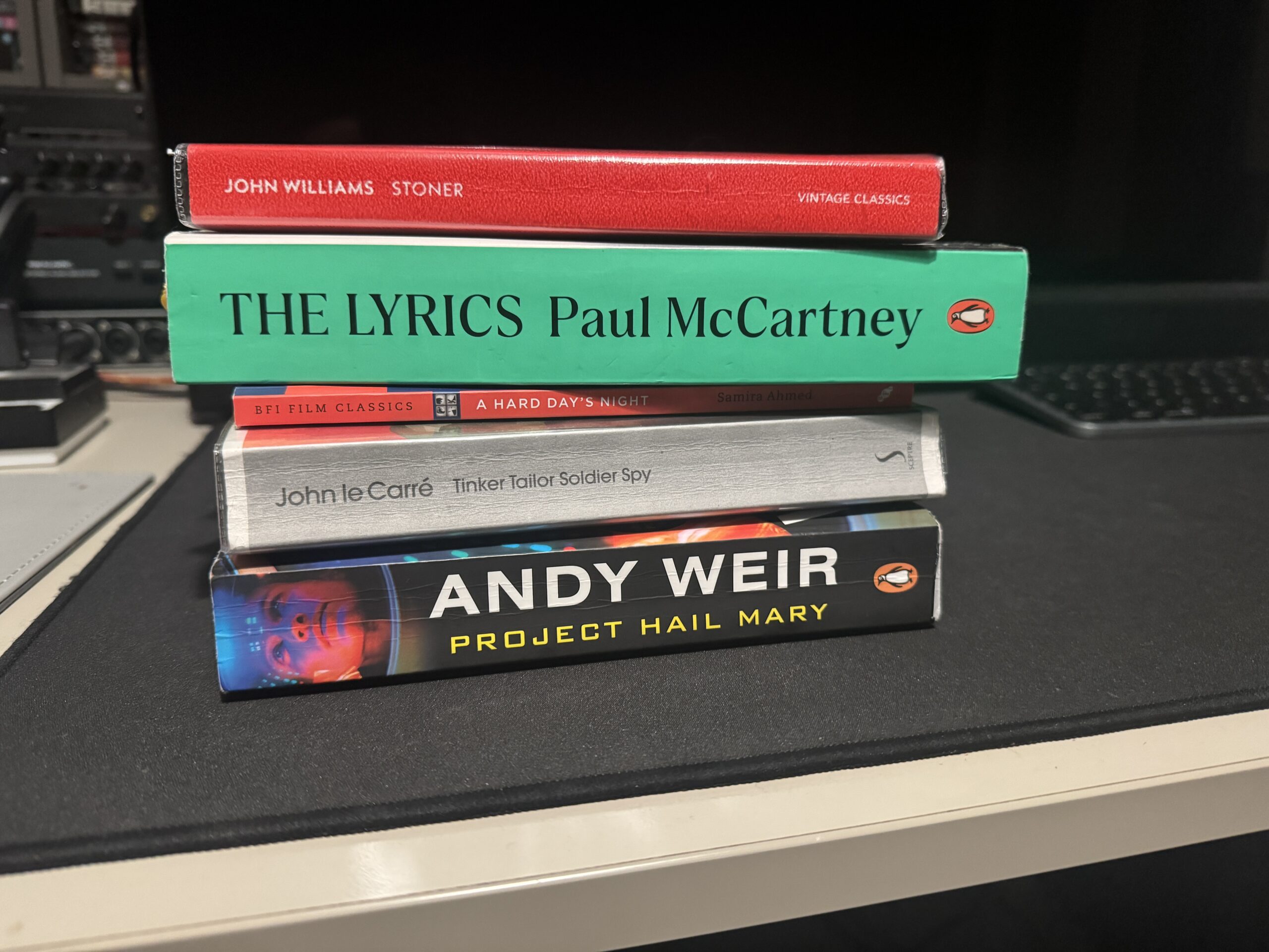 Some books from my reading list, stacked on top of each other. From top to bottom: Stoner, The Lyrics, A Hard Day's Night, Tinker Tailor Soldier Spy, and Project Hail Mary.